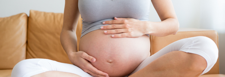 Woman sitting on sofa holding her pregnant belly