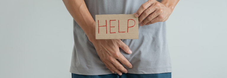 man holding a 'help' sign over his groin area to indicate sweaty balls