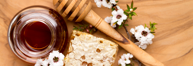 liquid honey, honeycomb, and honey spoon with manuka flowers