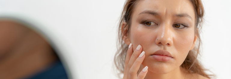 woman with concerned expression looking in mirror at dry skin on face