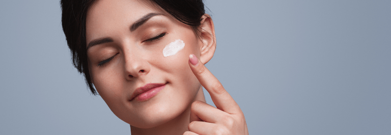 Woman with eyes closed and looking relaxed while rubbing in white cream under her eye.