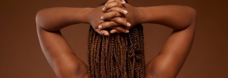 woman with dreadlocks, facing away from camera with hands on back of head