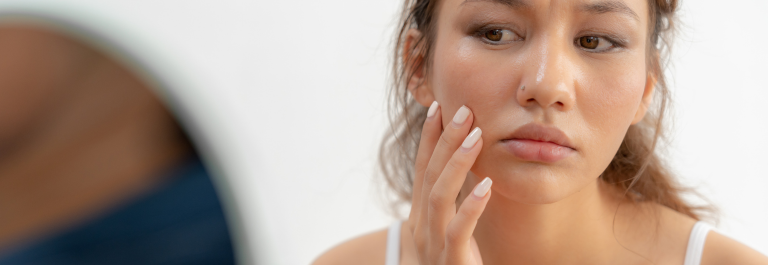 woman looking at face in the mirror with her hand around the mouth area